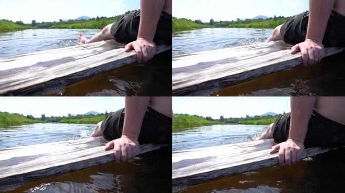 一个男人坐在一块木板上，把他的脚放在河里，享受着他的暑假