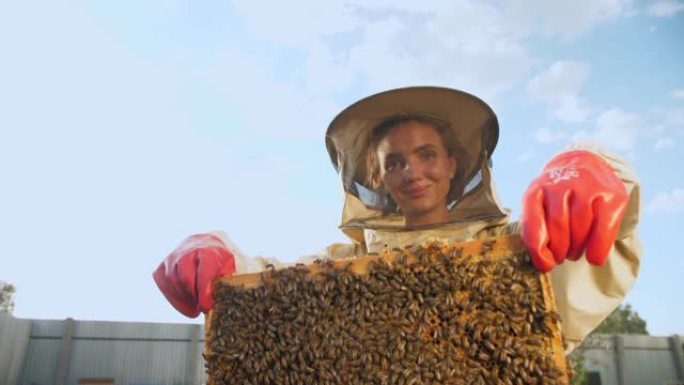 一个穿着防护服的女养蜂人带着蜂巢里的蜂蜜