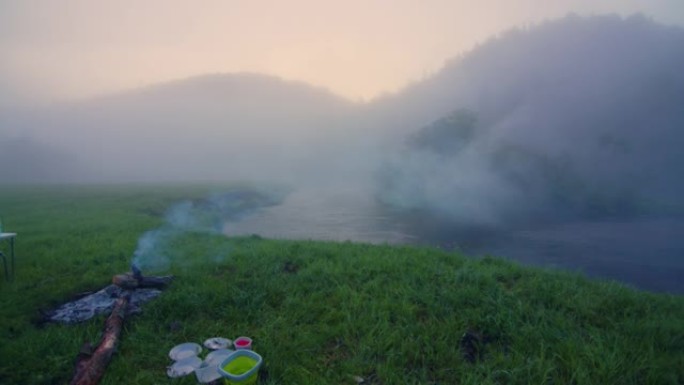 露营地，日出时有篝火和雾水，背景是山。俄罗斯乌拉尔山脉地区