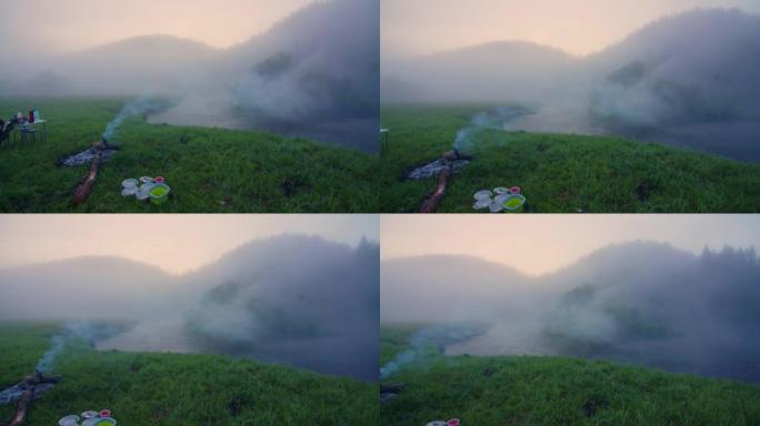 露营地，日出时有篝火和雾水，背景是山。俄罗斯乌拉尔山脉地区