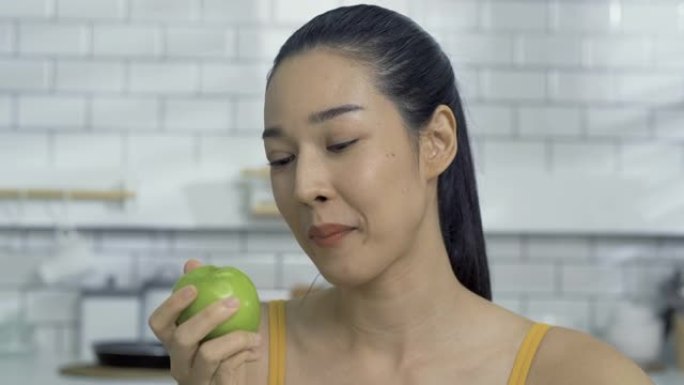 美丽的女人在厨房吃青苹果。