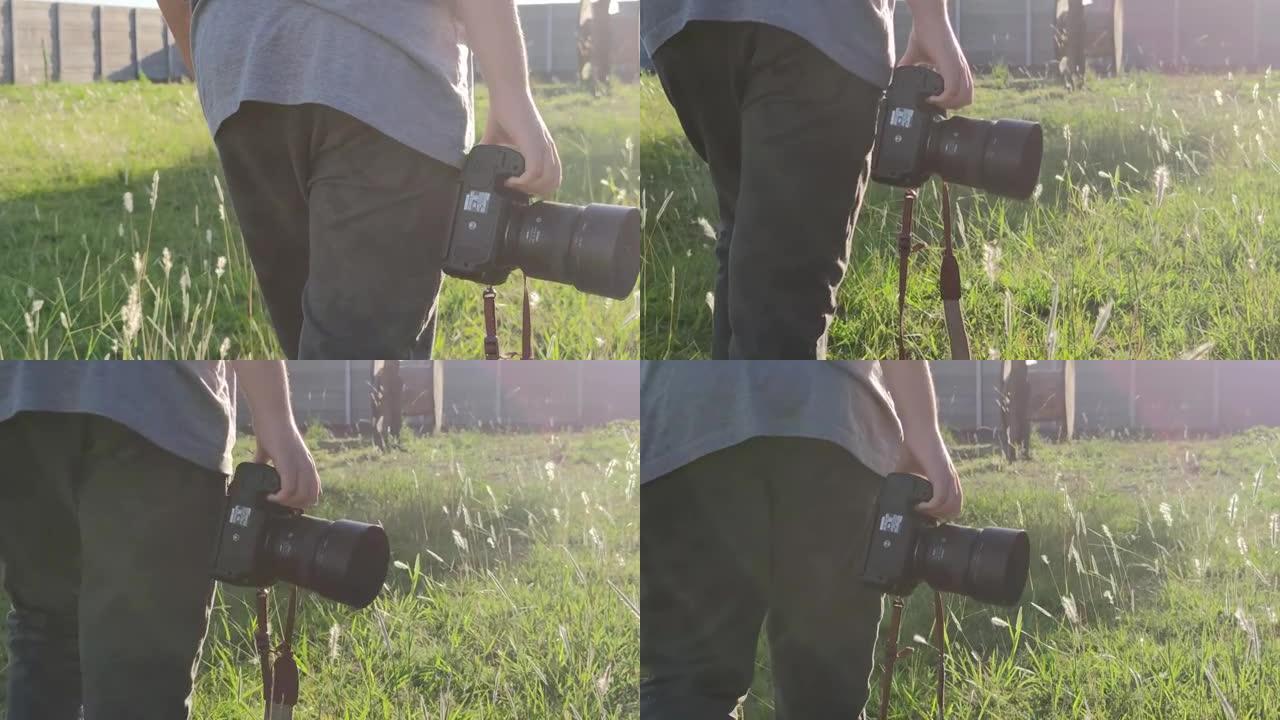 摄影师在背光的绿色草地上行走。手里拿着相机。