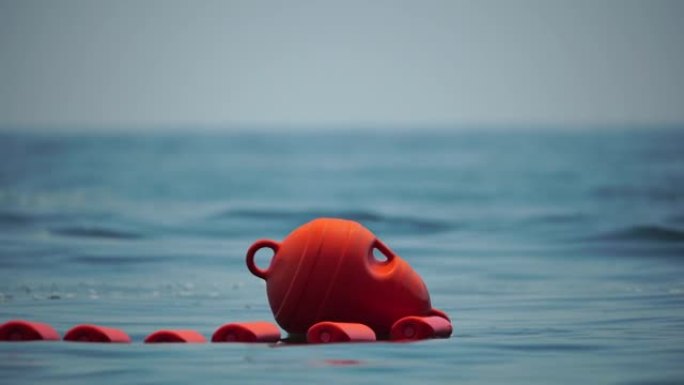 橙色的安全浮标漂浮在海上的绳子上，在一个阳光明媚的日子，关闭。海滩上游泳区的围栏