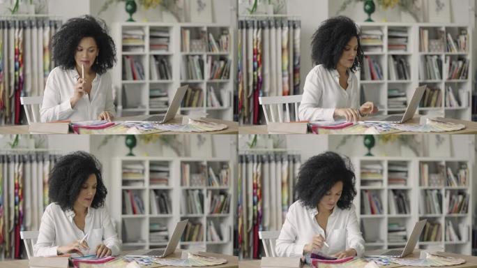 年轻的非洲裔美国妇女的肖像，通过调色板和面料样本寻找设计项目。女设计师坐在办公室的桌子旁。特写。慢动