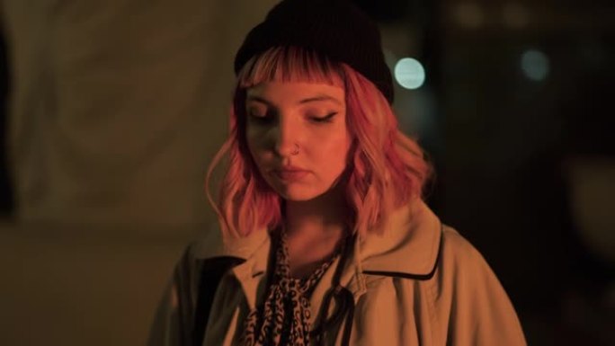 晚上在城市里看着相机的迷人粉红色头发的年轻女子的特写肖像