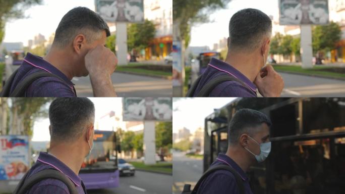 一名男子站在路边的公共汽车站等车时戴上医用口罩。