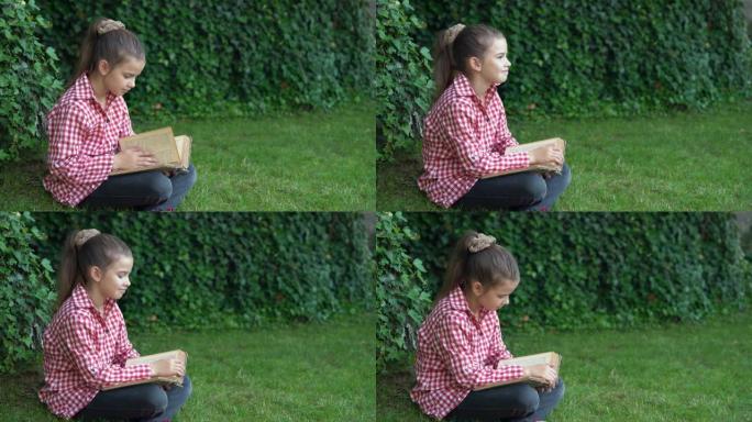 小狗女孩坐在公园的草地上读一本稀有的书。这孩子正在从大自然的教训中休息。年轻学生的教育和科学。小学生