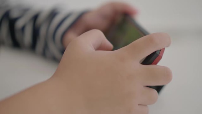 特写手亚洲小男孩在手机上玩游戏。用技巧移动手指
