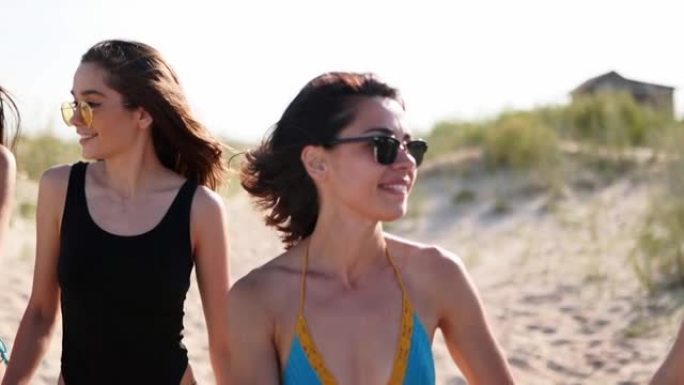 一群漂亮的女性朋友穿着泳衣在热带沙滩上散步很开心。夏季户外聊天和大笑的跨种族女性。海边穿着比基尼和泳