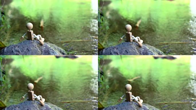 木制玩具独自坐在河景的岩石上。放松和孤独的概念。