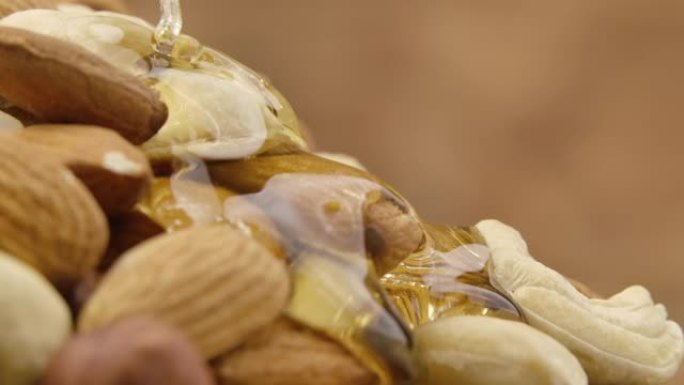 金色蜂蜜的涓涓细流从一堆坚果中缓慢流动。蜂蜜滴落并包裹杏仁，腰果和榛子的混合物。关闭甜糖浆中的坚果的