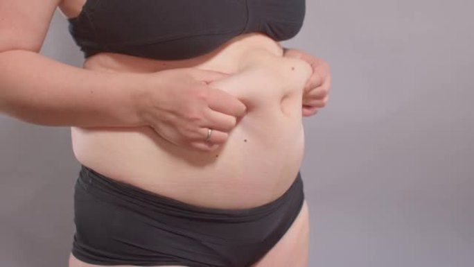 女人用手触摸胃，从脂肪组织中拉伸皮肤。
