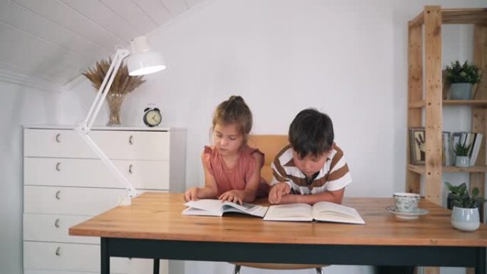 一个男孩和一个女孩坐在桌子上看书。孩子们正在做作业。家庭教育。自我隔离。儿童课程。慢动作