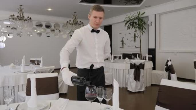 一家餐馆的一名戴着白手套的男服务员将红酒倒入玻璃杯中。