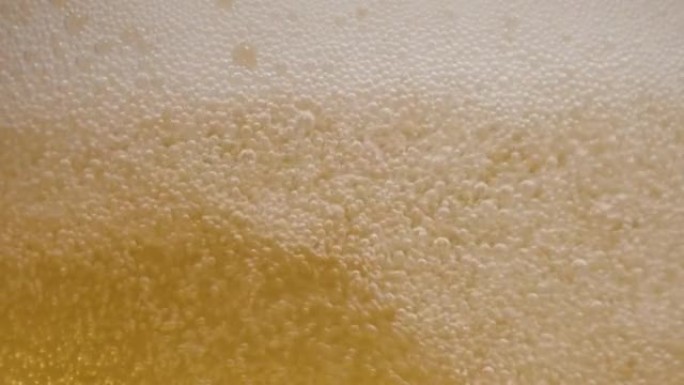 一杯啤酒内容物的特写。啤酒在玻璃，波浪，气泡和泡沫中缓慢地震动。