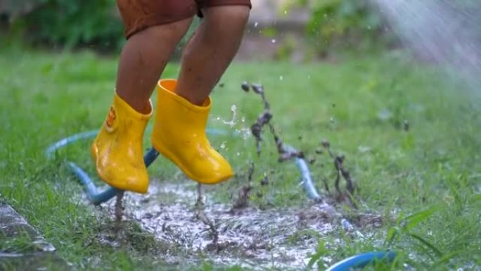 穿着靴子的亚洲孩子在公园玩泼水和泥泞。夏天和幸福的概念