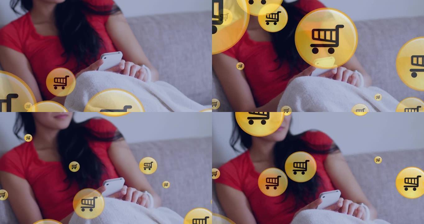 在家里的沙发上使用智能手机漂浮在亚洲女性身上的购物车图标