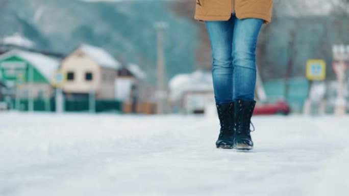 一名妇女小心翼翼地沿着积雪覆盖的小路行走，以免滑倒。底视图。腿的特写