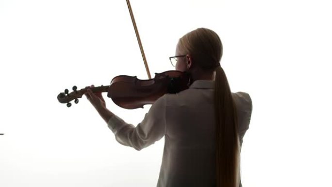 穿着白色上衣的女小提琴手拉小提琴，背站在工作室的白色背景上。音乐教育理念与爱好