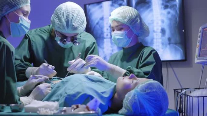 外科医生戴着双目放大镜，妇女协助挽救亚洲女性患者的生命，躺在医院手术室的床上，通过使用生命体征监视器