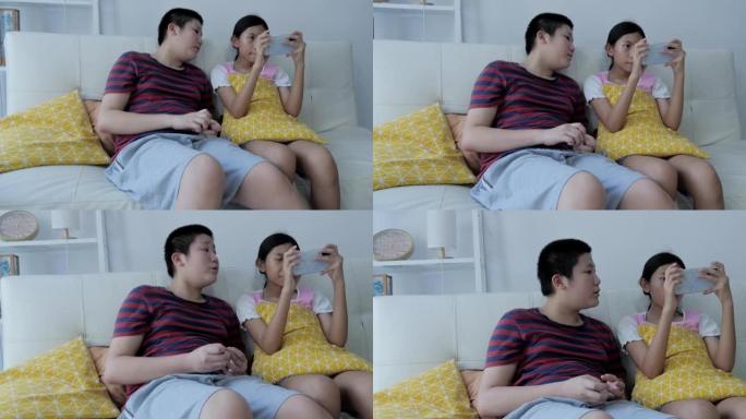 亚洲男孩看着他的妹妹在网上玩手机游戏，同时在家一起在沙发上放松，生活方式理念。