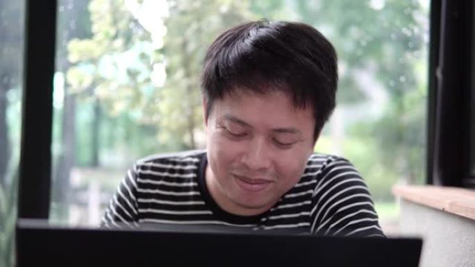 亚洲人坐在咖啡店里用笔记本电脑工作。