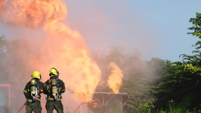 消防员或消防员的侧视图在工作场所训练期间，练习从现场的管道向火中喷水