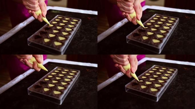 厨师糕点巧克力的特写镜头将液态奶油馅料倒入巧克力模具中，在家中准备美味的手工果子理。世界巧克力日。烹