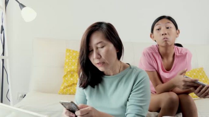 强调母亲在家和女儿在沙发上使用智能手机在家制作电子银行账单，生活方式概念。
