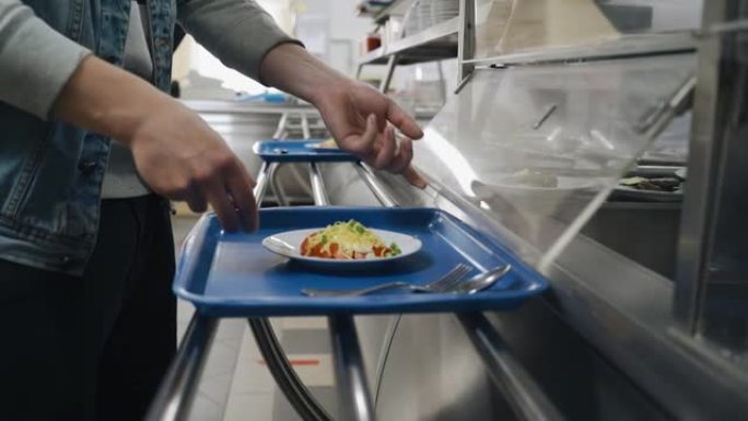 饭厅分配台上的人把食物放在托盘上。并排特写