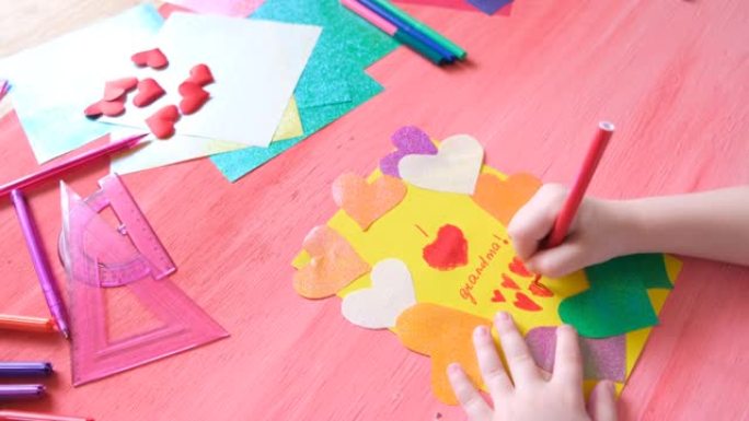 小女孩给奶奶做卡片。彩色粉色背景，纸质装饰，五彩心形。生日、母亲节和祖父母节的手工制作概念