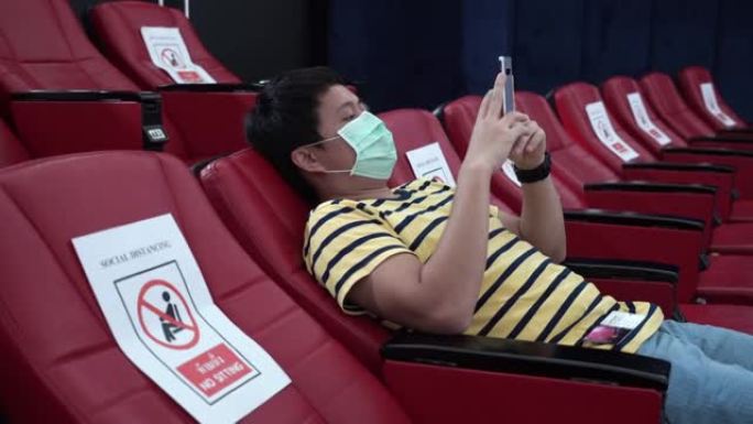 亚洲男子在冠状病毒大流行期间在电影院戴防护口罩。