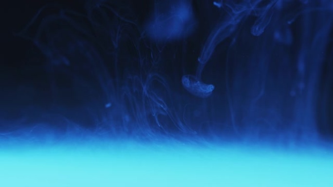 浅蓝色色调烟雾状背景上悬浮在水中的白色墨水
