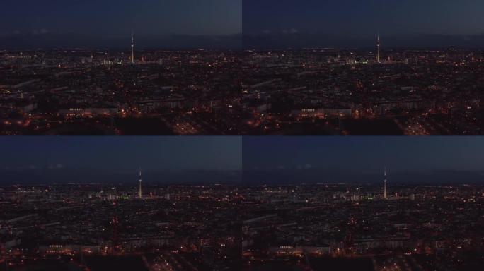 晚上飞越大城市。城市社区和城镇占主导地位的高而薄的电视塔Fernsehturm的鸟瞰图。德国柏林