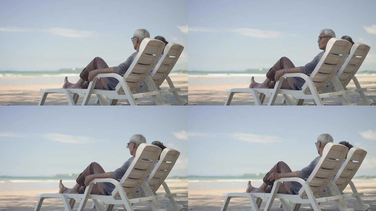 在海滩上休闲活动的高级夫妇的后视图，高级妻子，高级丈夫坐在沙滩椅上，在暑假那天退休后在树荫下放松景观