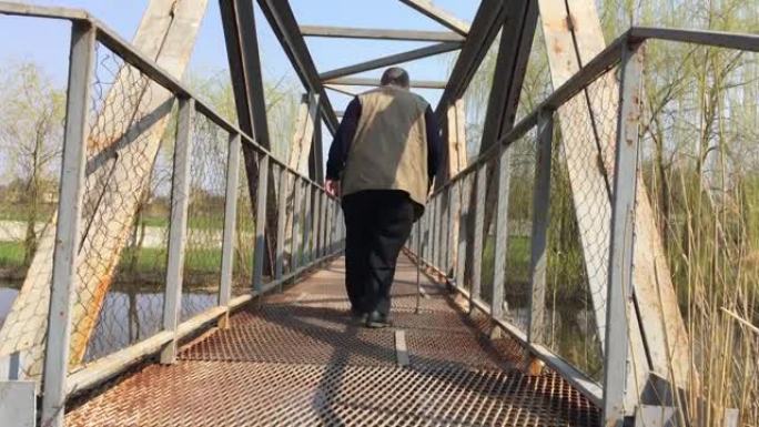 残疾的大胡子老人，手杖在小河上的金属桥上缓慢移动