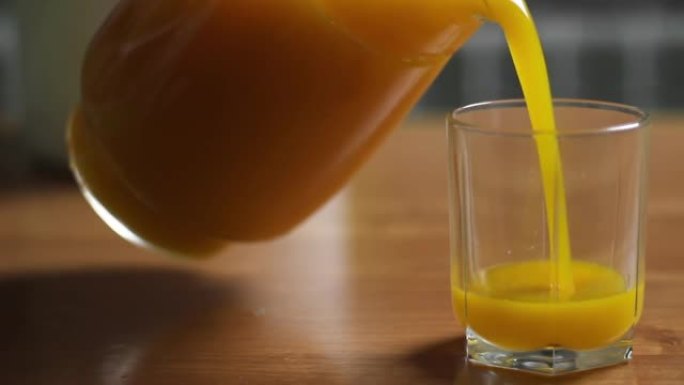 将橙汁或南瓜汁从水罐倒入玻璃杯中