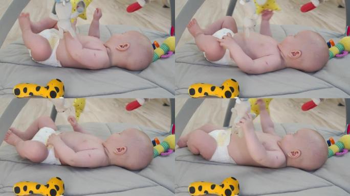 可爱的男婴抓住并拿着悬挂的玩具摇铃躺在游戏垫上，发展伸展手臂和抓住东西的能力，3个月大的新生婴儿。