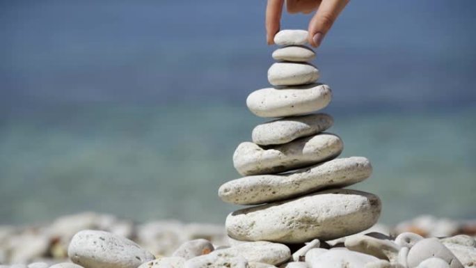石头平衡特写。用海石手工制作鹅卵石塔的女性。海滩上鹅卵石金字塔的宏。