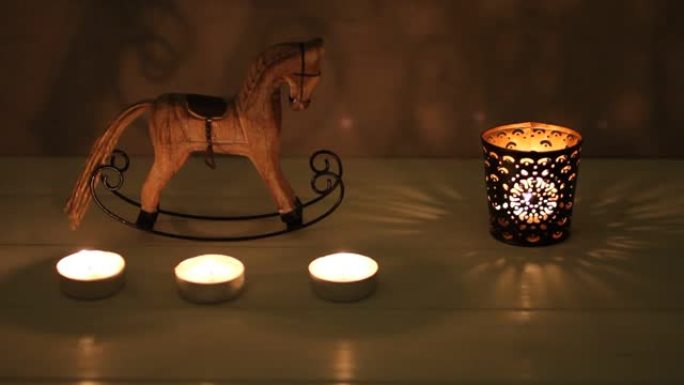 圣诞装饰-木制玩具摇摆-白色木桌烛台上的马和蜡烛。背景中的混凝土墙。晚上摄像。特写