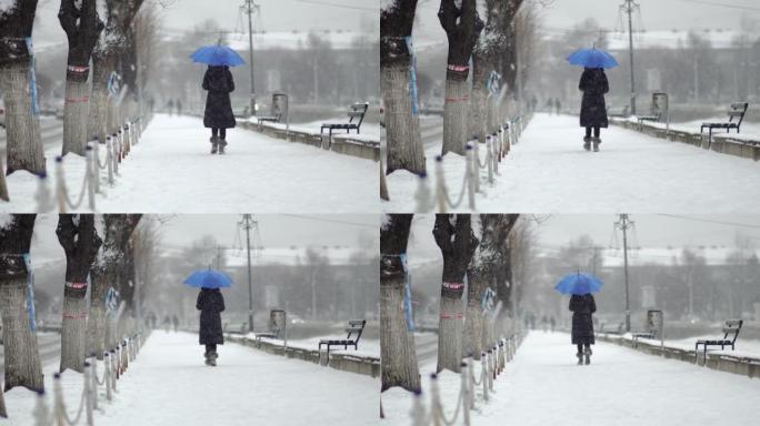 下雪时，年轻女子在公园里打着雨伞走在人行道上，暴风雪使一切都变白了