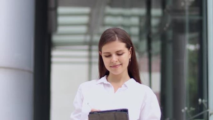 漂亮年轻的笑脸女商人在办公室外使用现代平板电脑。一位美丽的女性潮人的肖像为她的视频博客录制了一段视频