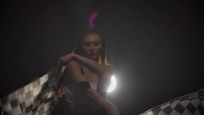 性感黑发女子挥舞着方格黑白种族旗帜的肖像。一个年轻女子的剪影在一个带背光的黑暗烟熏工作室里摆姿势。特