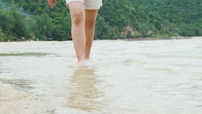 夏季赤脚独自在沙滩上行走的特写，女性的脚踩在海上