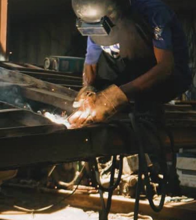 垂直工业工厂机械工人man钢焊工在工业工厂戴焊接面罩焊钢。