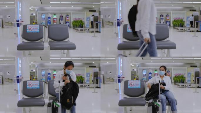 4k亚洲旅游女性戴着防护卫生口罩，冠状病毒带着旅行包和背包散步，坐在机场的社交距离椅上。新常态概念。
