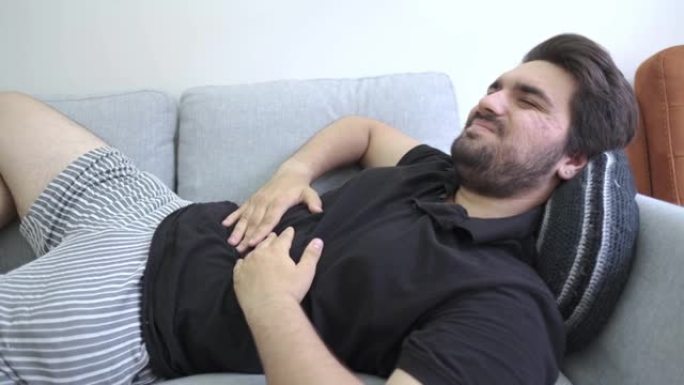 一个年轻人躺在沙发上抱住肚子的胃痛