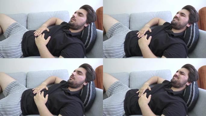 一个年轻人躺在沙发上抱住肚子的胃痛