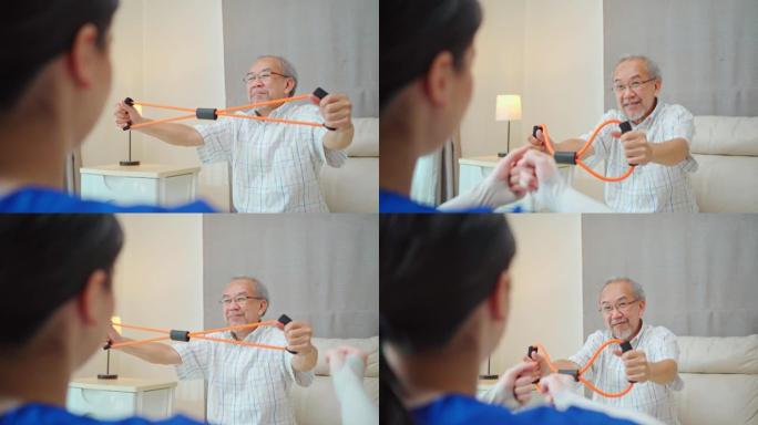 亚洲残疾老年男子坐在沙发上，在治疗师护士的支持下做理疗师。老年残疾人在家庭护理中使用阻力拉伸带运动对