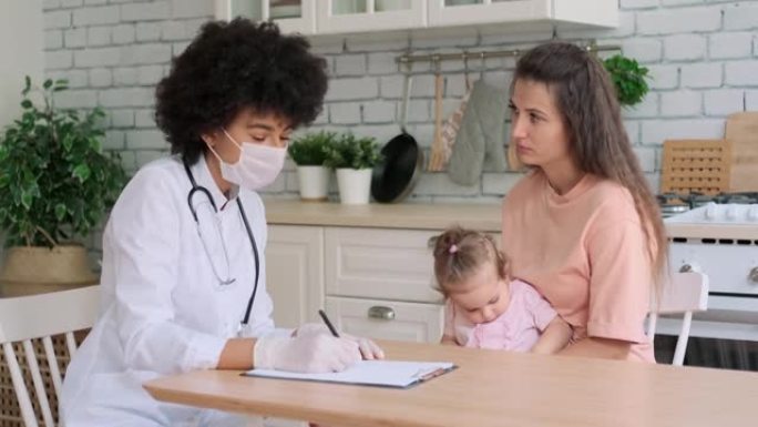 戴着面具的非裔美国女医生在家里检查一个生病的小女孩时写处方